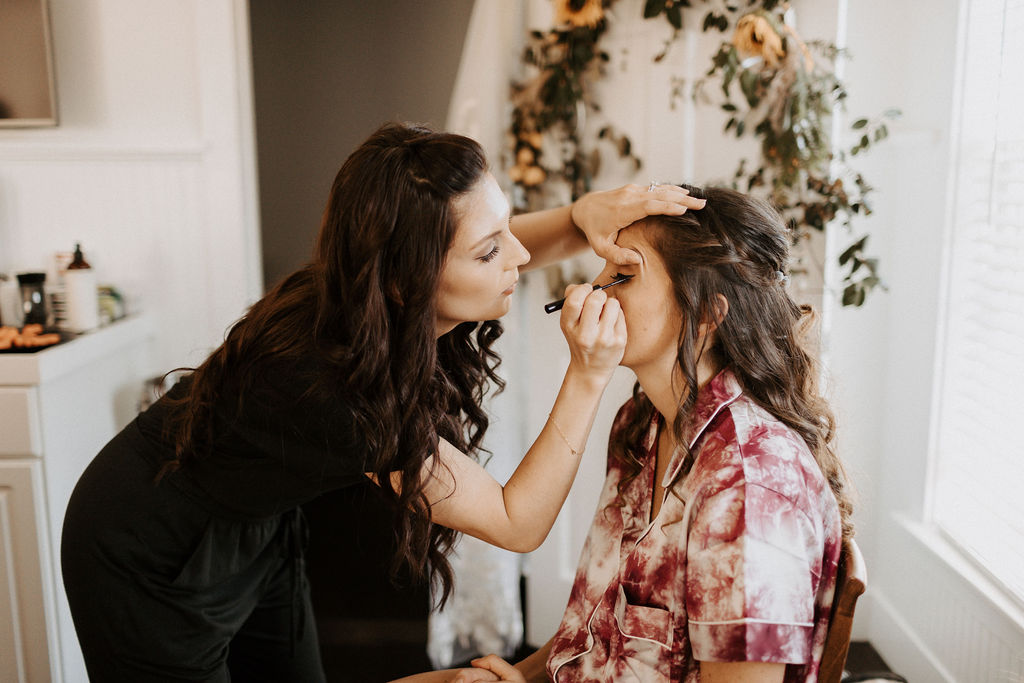a woman puts makeup on a bride.