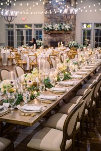 Reception table set with candles, white roses, and greenery under warm vineyard lighting.
